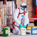 Industrial worker in protective gear handling chemicals in a warehouse environment.