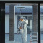 A man in full protective gear cleaning a glass window during the daytime.